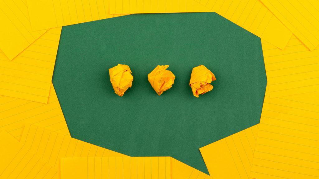 three crumpled pieces of yellow paper in green paper speech bubble