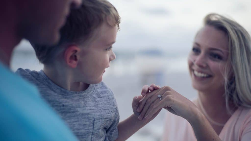 Father holding his young son, who's holding his smiling mom's hand