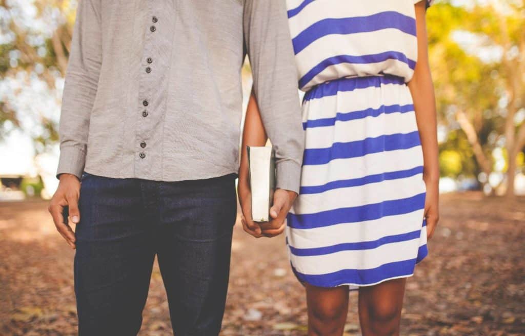 Close up of young couple holding hands which are also holding a Bible together. The couple's heads are not shown.