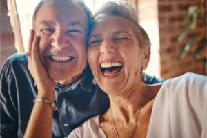 A husband and wife facing the camera, laughing together, embodying the phrase “laughter is the best medicine.”