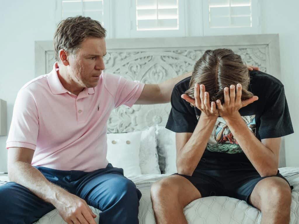 Dad sitting with son who has head in hands