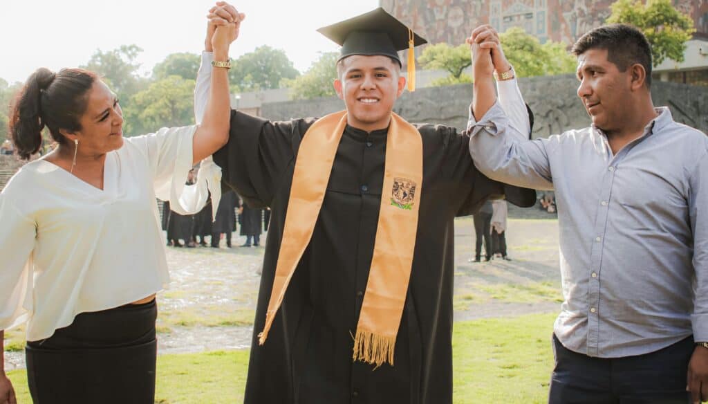 graduate with parents proud raising arms