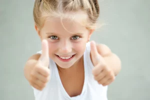 Girl with her hair in braids smiling and giving a thumbs up