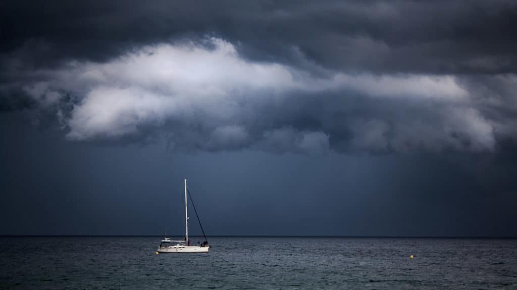 Boat sailing under dark sky and stormy clouds