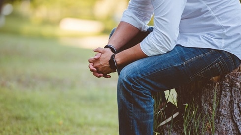 Man sits thoughtfully on stump outside