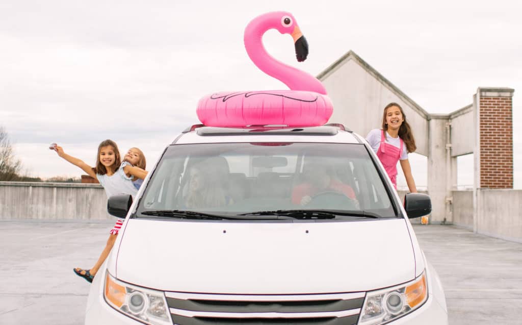 A photo of a family in a parked car. The children are excited and leaning out of the car.