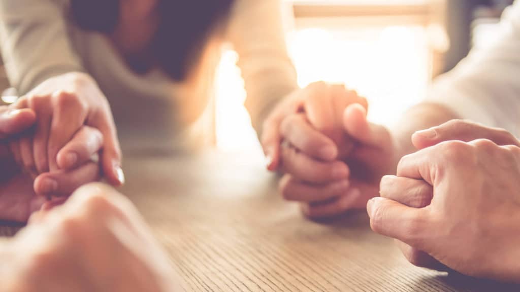 A group of men and women hold hands and pray