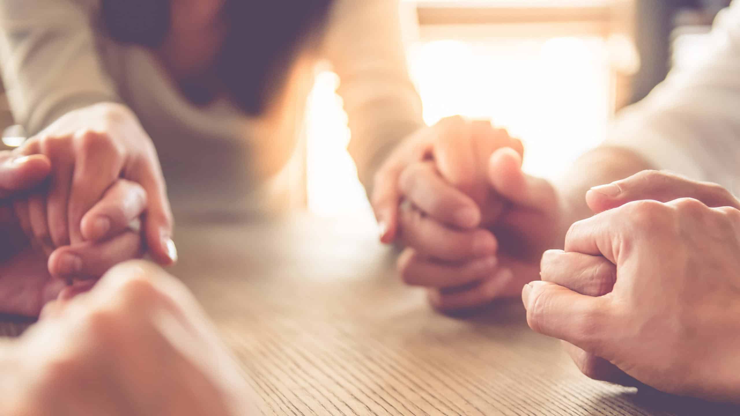 A group of men and women hold hands and pray