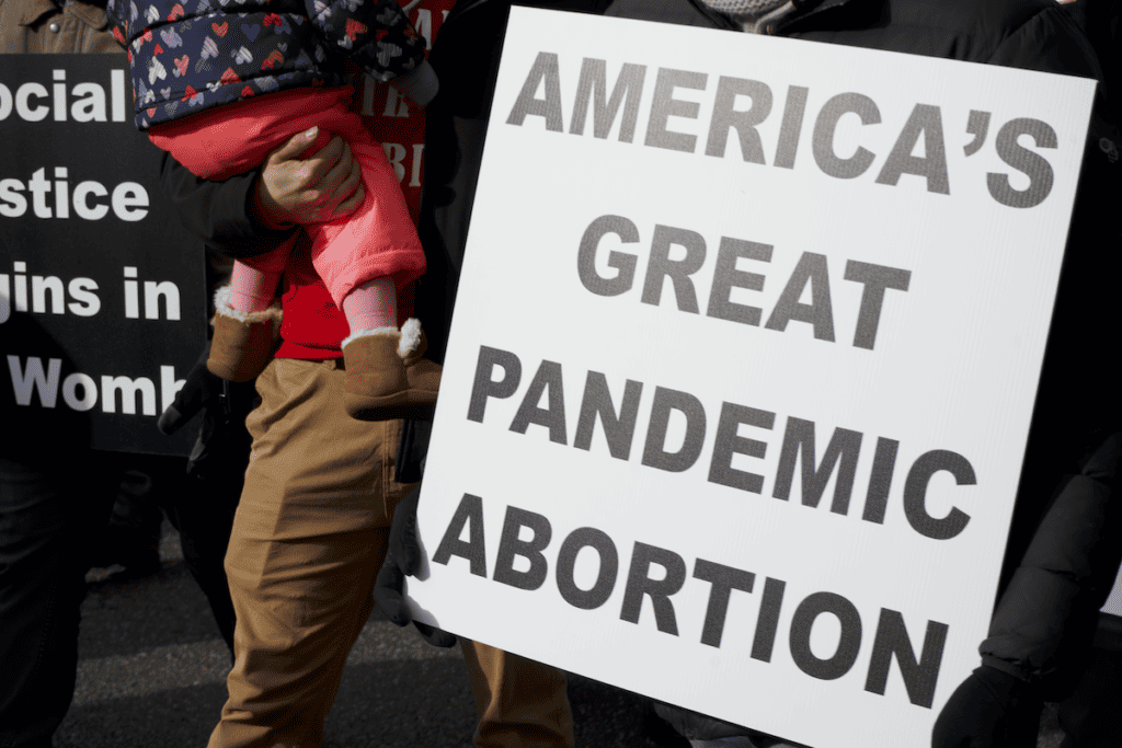 A march for life sign saying "America's great pandemic abortion"