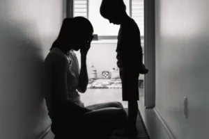 Mom sitting on floor in hallway, crying while child looks on