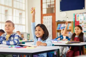 Little girl with big grin raising her hand in school