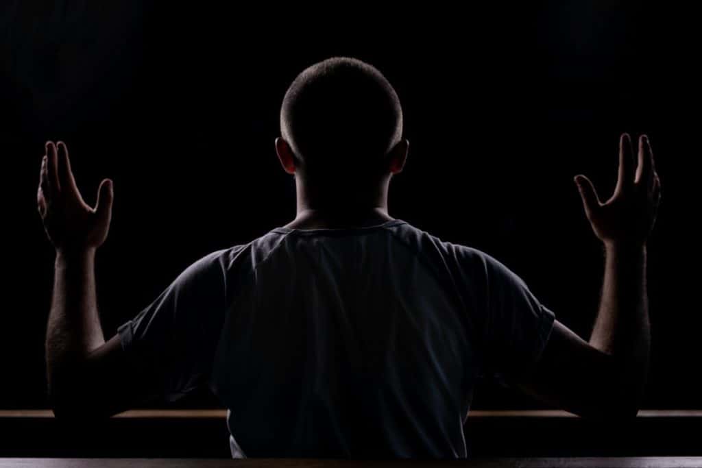 Photo of a man praying in the dark, hands lifted in the air.