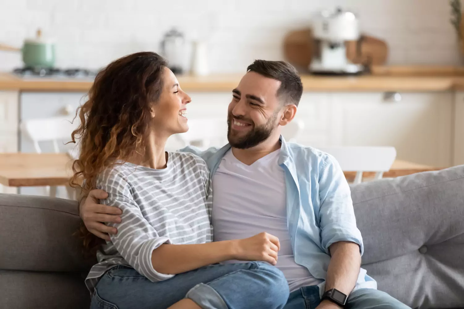 A young couple sit on the couch with their arms around each other. Validation in your marriage is key to conflict resolution.