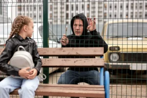 man in hoodie talking to a young girl through a school wire fence