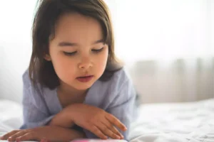 Teach your children biblical prayer. Little girl laying on her bed reading her bible.