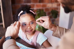 Will homeschooling make my kid weird? Pretty little girl with pink clips in her hair, and her dad fitting her pink glasses on her face as she smiles.